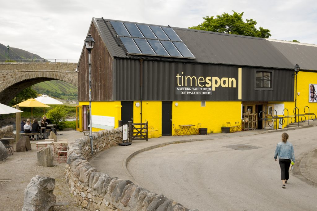 Picture of outside of Timespan museum - brown top half and yellow bottom half of building with the letters in yellow of the name (timespan) across the brown wood on the top half