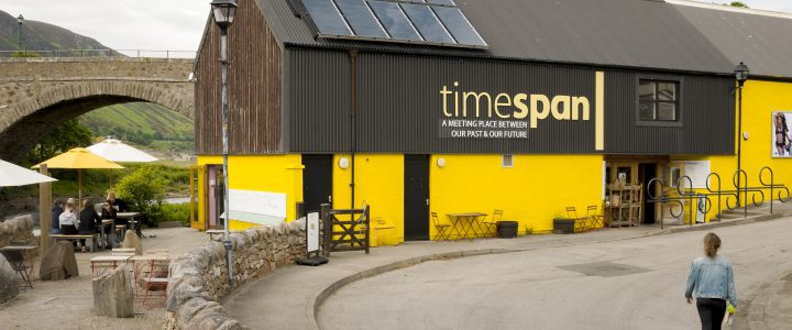 Picture of outside of Timespan museum - brown top half and yellow bottom half of building with the letters in yellow of the name (timespan) across the brown wood on the top half