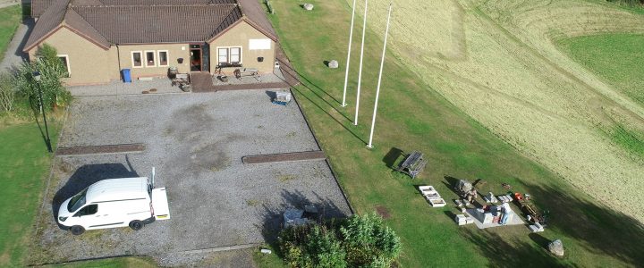 A picture of Brora heritage centre taken from the sky above. Shows the brown building surround by green fields and a white van in the car park