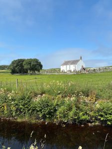 View of Strathnaver Museum, housed in a white former parish church, set within a rural landscape near Bettyhill under a blue summer sky.