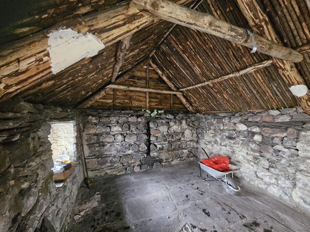 Interior of a traditional stone and timber building showing exposed wooden roof timbers, stone walls and a stone floor during clearance works